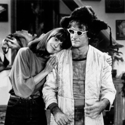 American comedian and actor Robin Williams, wearing a woman's bathrobe, furry hat, and sunglasses, being hugged by American actor Pam Dawber, in a still from the television series, 'Mork and Mindy'.
