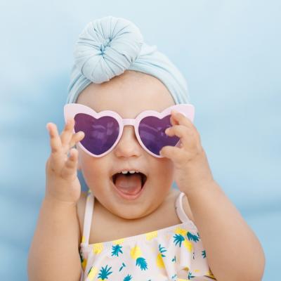 Baby wearing a turban and heart sunglasses on a blue background.