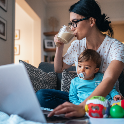Mom with a baby drinking coffee while working at home with a laptop