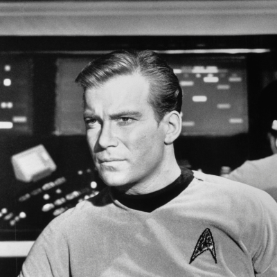 William Shatner as Captain James Kirk with a look of concern in close up of him seated in the Starship Enterprise in an episode of "Star Trek".