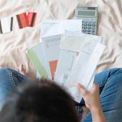 A person holding bills and receipts with credit cards and a calculator nearby.