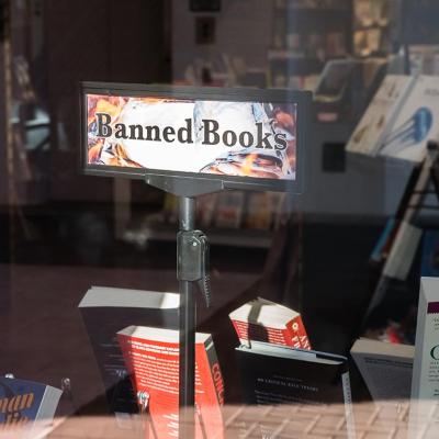 View of bookstore window where a "banned books" sign is displayed above books for sale.