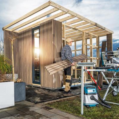 Woodworker with equipment building a modern backyard garden shed.