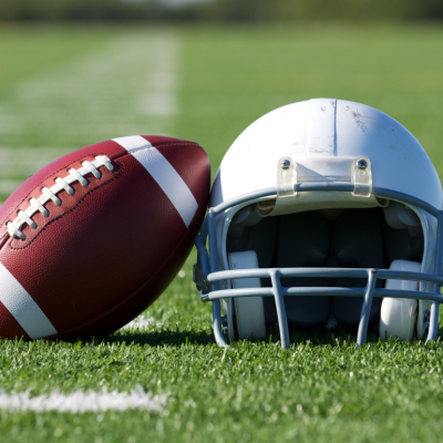 A football is propped against a helmet on a football field.