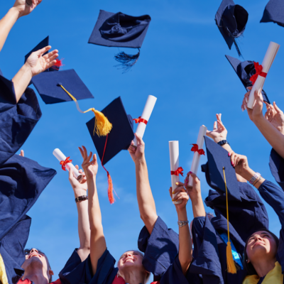 Students at a high school graduation holding diplomas and throwing graduation caps.