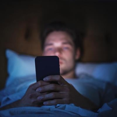 A man browsing on a smartphone while lying in bed at night.