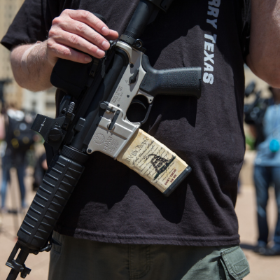 Person with an assault rifle across their chest, a miniature copy of the American constitution on the gun handle, at a counter-protest by gun advocates in response to protesters opposing the NRA's annual convention in Dallas, Texas, 2018.