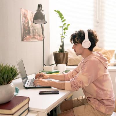Person wearing headphones and pink tie-dye sweatshirt works peacefully on laptop in room with window light.