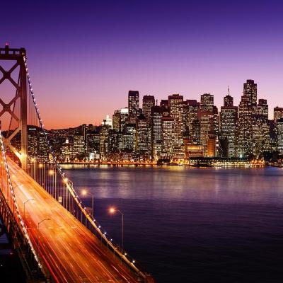 San Francisco skyline at dusk with bay bridge visible in the foreground.