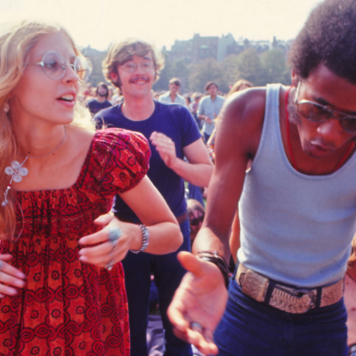 Two young people dancing and clapping in a park in the 1960s.