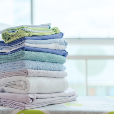 A stack of folded clean laundry sites on an ironing board.