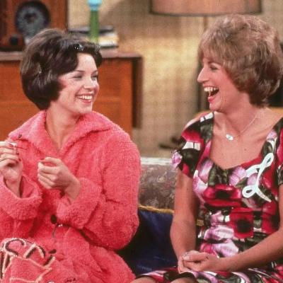 Actors Cindy Williams and Penny Marshall sit on their sofa laughing in a still from 'Laverne and Shirley.'