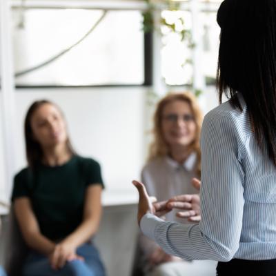 A female counselor facing a group of women and engaging them in a discussion.