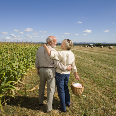 Senior couple standing next to a cornfield embracing and smiling at each other.