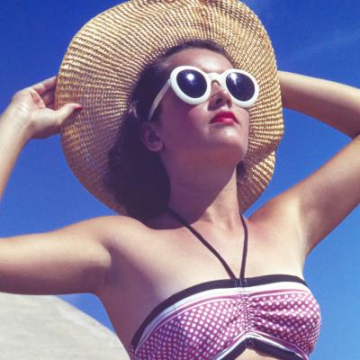 Person wearing sunglasses and a wide-brimmed hat sunbathing in 1944.