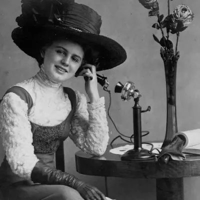 Woman with hat seated at table talking on early standing telephone