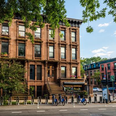 Scenic view of a classic Brooklyn brownstone block with a long facade and ornate stoop balustrades on a summer day in Clinton Hills, Brooklyn.