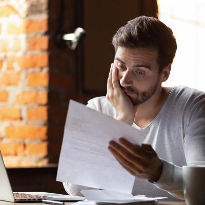 A man working with his laptop while reading a file in deep wonder.