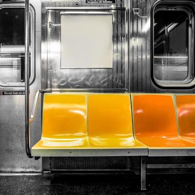 A black and white photograph inside a subway train but the seats are colored in yellow and orange.
