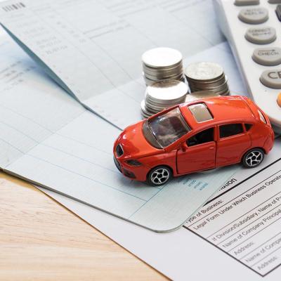 Car insurance bills are seen with a red toy car, coins and a calculator on top of it.