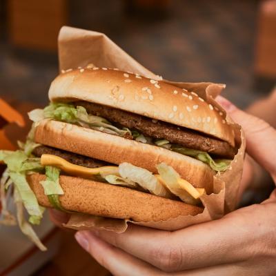 Double cheeseburger in customer's hands at fast-food restaurant.