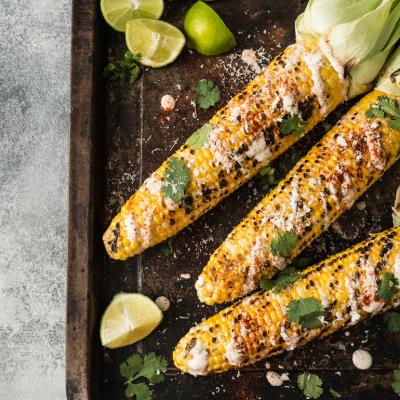 Grilled corn cobs with sauce, coriander, lime, paprika, and cheese.