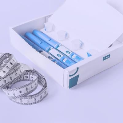 Box of semiglutide injectable drugs and measuring tape on lavendar background.