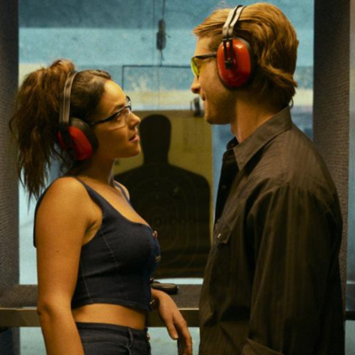 Adria Arjona and Glen Powell facing each other in a gun range in a scene from Netflix movie 'Hit Man'