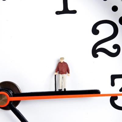 Concept of longevity illustrated by clock with miniature old man figurine place on the hour hand.