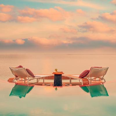 Pink and pastel sunset from the point of view of an infinity pool with two chairs looking out onto the ocean. 