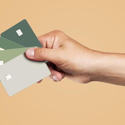 A person's hand is holding four credit cards displayed over a beige background.