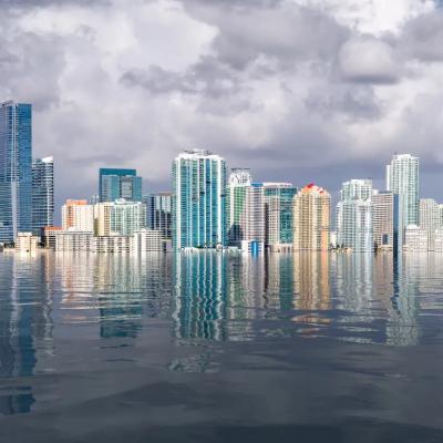 City skyline dots cloudy sky over flooded sea.