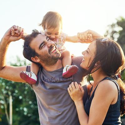 A small child sits on a man's shoulders while a woman makes faces and laughs along.