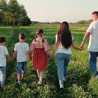 Family of five holding hands seen from the back, walking through a grassy field.