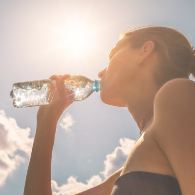 Woman drinking water out of a plastic bottle on a hot sunny day