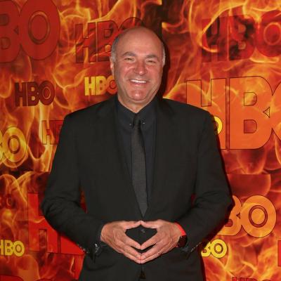 Kevin O'Leary poses in front of a red and orange HBO step-and-repeat background.