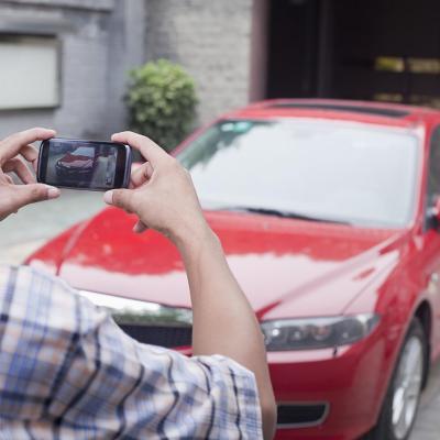 Young person in foreground taking photo of a red car from the front with a smartphone.