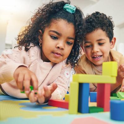 Two children and laying on their stomachs on the floor with toys for playing with building blocks.