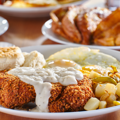 Chicken fried steak covered in gravy with sunny side up eggs, biscuits and potatoes on a plate