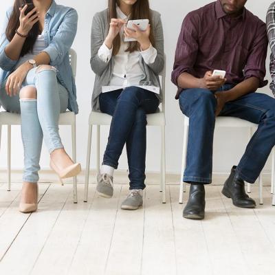 A group of five students sitting in a waiting room, all using their devices.