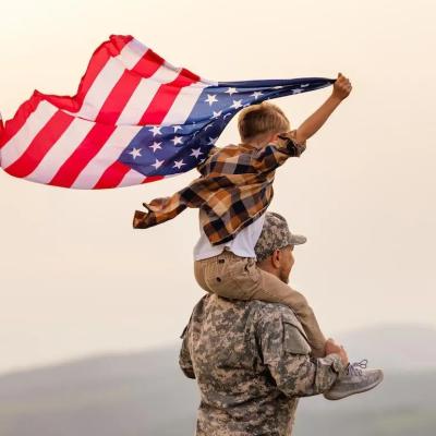 Military soldier carrying child with an American flag on shoulders.