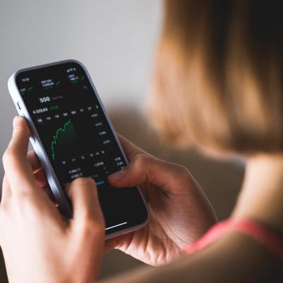 Woman seen from behind, holding a phone investment app showing index growth chart.