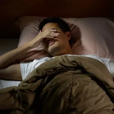 Person lying in bed in the dark with a hand over their eyes