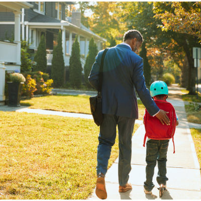 Parent walking with child on the sidewalk in the suburbs.