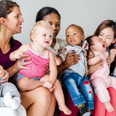 A group of five parents are sat and each one is holding their little child.