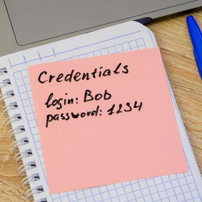 Simple user and password credentials written on a sticky note that lies on a notebook next to a laptop. 