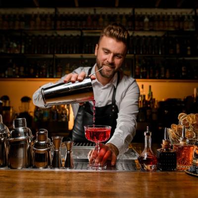 Bartender pours a cocktail from a steel shaker into a glass.