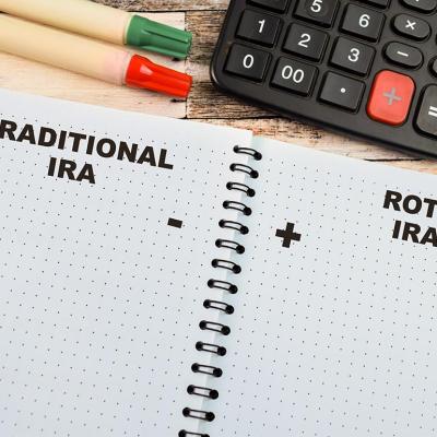 Concept of Traditional IRA and Roth IRA depicted on paper list in notebook on a wooden table with blank columns for pros and cons.