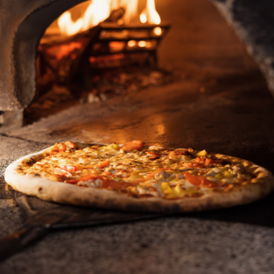 A freshly-baked pizza being pulled out of a wood-fire oven