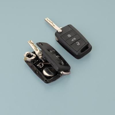 Broken damaged car key gob and new remote vehicle key side by side against pale greenish grey background.  